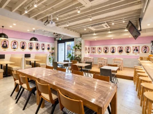 木のテーブルとカウンターが並ぶ、ピンクの壁の店内